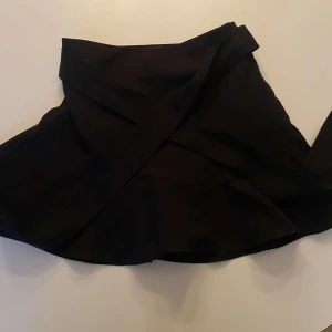 Svart omlottkjol från Zara - Snygg svart omlottkjol från Zara i en stilren design. Perfekt för att skapa en chic look. Kjolen har en omlottstil som ger en modern touch.