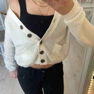 Vit stickad kofta från H&M - Säljer en vit stickad kofta från H&M med stora knappar och två fickor framtill. Koftan har en v-ringad design och långa ärmar. 💓