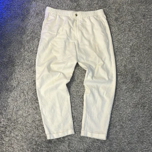Vita linnebyxor från H&M - Snygga vita linnebyxor från H&M i regular fit. Byxorna har en avslappnad stil med elastisk midja och knappar bak. Perfekta för en somrig look. Knappt använda.