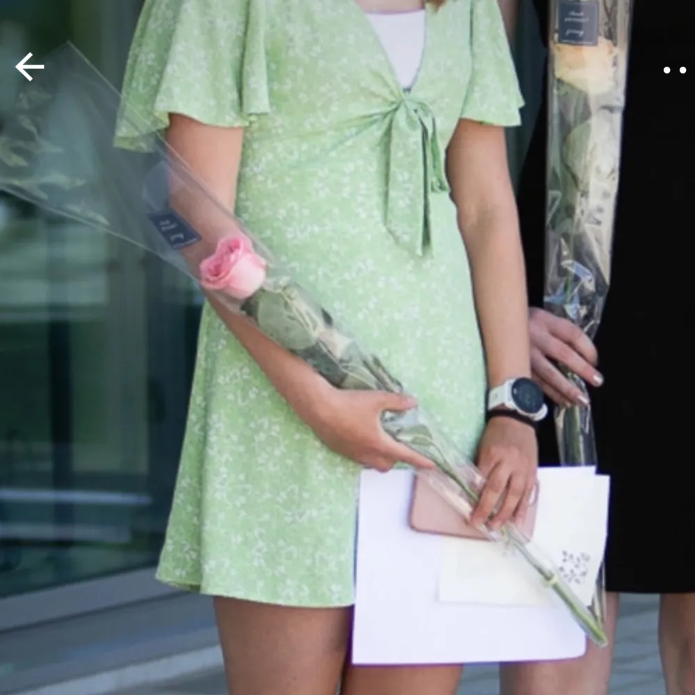 Säljer en söt grön klänning med blommigt mönster och korta ärmar. Klänningen har en v-ringad design med knytning framtill och volangdetaljer vid ärmarna.. Mekot.