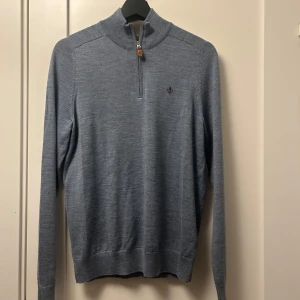 Grå stickad tröja med dragkedja - Snygg grå stickad tröja med halv dragkedja och ett litet broderat emblem på bröstet. Perfekt för kyligare dagar med sin stilrena design och långa ärmar. Passar både till jeans och chinos för en avslappnad look.