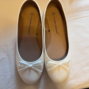 Vita ballerinaskor från Claudia Ghizzani - Snygga vita ballerinaskor från Claudia Ghizzani med en söt rosett på ovansidan. Perfekta för en stilren look. Skorna har en rund tå och en bekväm passform.