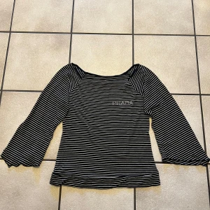 Svartvit randig topp  - Snygg svartvit randig topp med trekvartsärmar. Perfekt för en stilren look. Toppen har en klassisk design med en liten logga på bröstet.