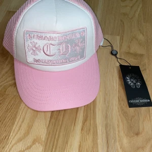 Rosa och vit keps från Chrome Hearts - Snygg keps i rosa och vitt från Chrome Hearts med broderad logga framtill. Kepsen har ett justerbart spänne baktill och är perfekt för en avslappnad stil.
