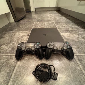 PlayStation 4 med två handkontroller - Säljer en PlayStation 4 med två svarta DualShock 4-handkontroller. Konsolen har en stilren design och kommer med nödvändiga kablar. Perfekt för gamingkvällar med vänner! 🎮