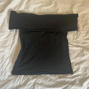 Svart axelbandslös topp - Snygg svart axelbandslös topp som passar perfekt för en stilren look. Toppen har en enkel design och är gjord i ett mjukt material som sitter bekvämt mot kroppen.