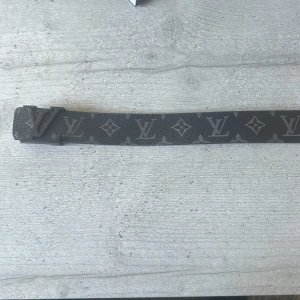 Svart bälte från Louis Vuitton - Snyggt svart bälte från Louis Vuitton med det klassiska LV-mönstret. Bältet har en stilren design med en matchande svart spänne. Perfekt för att ge en lyxig touch till din outfit. Har kvitto