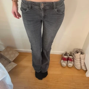 Grå jeans med låg midja - Snygga grå jeans med låg midja och bootcut-stil. De har dubbla knappar fram och fickor med lock bak. Perfekta för en avslappnad look.