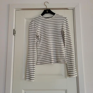 Vit och svart randig tröja - Säljer en stilren vit tröja med svarta ränder. Tröjan har långa ärmar och är ribbad, vilket ger en skön passform. Perfekt för en avslappnad look.