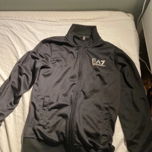 En svart Armani tracksuit  - En svart Armani tracksuit i storlek 140. På Tröjans dragkedja har det lossnat en bit. Det är en liten färg fläck på tröjans rygg men lnget man lägger märke till