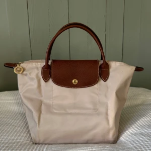 Beige handväska - Snygg handväska som är köpt second hand, men som tyvärr inte kommit till användning. Skick: okej - har småfläckar här och var, men ej något man ser på långt håll. Har även en lite större fläck på undersidan (se bilder) Höjd: 30 cm. OBS: då jag har köpt den begagnad kan jag inte garantera att den är äkta. Jag tror att den är det men jag är ej säker, därav lågt pris. ☺️