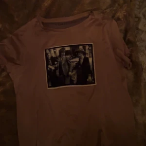 Limitato t shirt - Säljer en brun t-shirt med ett svartvitt tryck på framsidan. T-shirten har korta ärmar och en rund halsringning. Perfekt för en avslappnad stil.