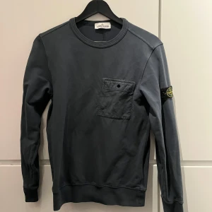 Mörkgrå tröja från Stone Island - Snygg mörkgrå tröja från Stone Island med en bröstficka och knappdetalj.
