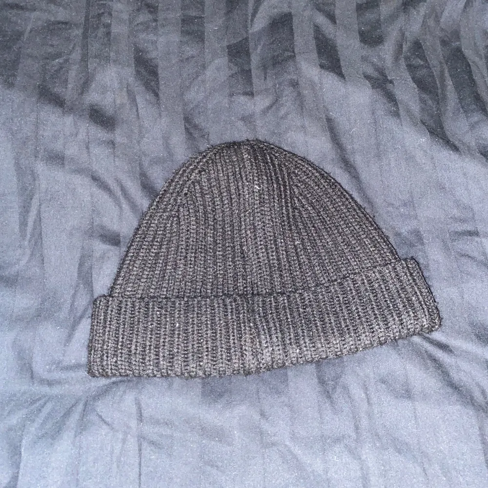 Snygg svart ribbstickad mössa från C.P. Company med unika glasögondetaljer framtill. Perfekt för att ge din outfit en cool touch. Tillverkad i ett mjukt och bekvämt material.. Asusteet.