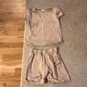 Beige shorts med stänkmönster - Säljer ett par pyjamas shorts och pyjamas tröja i ett set med ett coolt svart stänkmönster. Shortsen har en elastisk midja för extra komfort. Perfekta för en avslappnad stil. Säljer då de inte passar