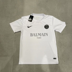 PSG Balmain tshirt  - Tja säljer nu denna riktigt fräscha Psg x Balmain tischa. Den är aldrig använt, alltså helt ny! Armhåla till armhåla 48cm, längd 70cm. Riktig snygg tischa nu till varmare tider! Bara att fråga vid eventuella funderingar mvh