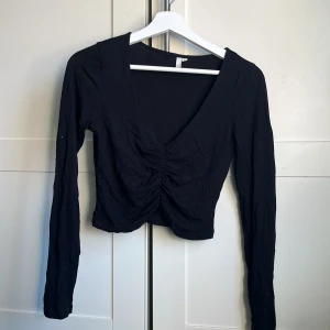 Svart långärmad topp - Säljer en svart långärmad topp med v-ringning och rynkad detalj framtill. Perfekt för en stilren look.