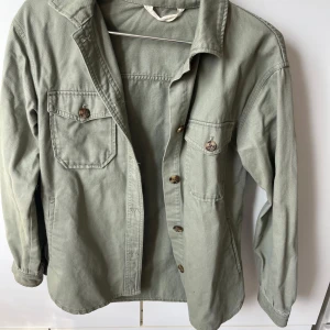 Grön overshirt med knappar - Säljer denna fina skjortjackan från H&M. jättefint skick och perfekt nu till våran. Använd men inga tydliga defekter.🩷