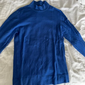 J.Lindeberg Blå merinoull polotröja. storlek S herr - Säljer en stilren blå polotröja i 100% merinoull från Newman Turtle. Tröjan har långa ärmar och en klassisk polokrage, perfekt för kyligare dagar. Den är mjuk och bekväm, vilket gör den till ett utmärkt val för både vardag och mer uppklädda tillfällen.