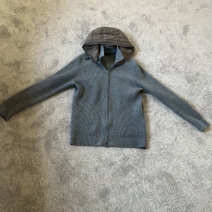 Grå stickad jacka med quiltad huva från Massimo Dutti - Snygg grå stickad jacka från Massimo Dutti med quiltad, avtagbar huva i mörkare grått. Jackan har dragkedja framtill och är ribbstickad för en modern look. Perfekt för sommarkvällar . Nypris 6000 skick 9/10 med en väldigt bra passform, size L fits M