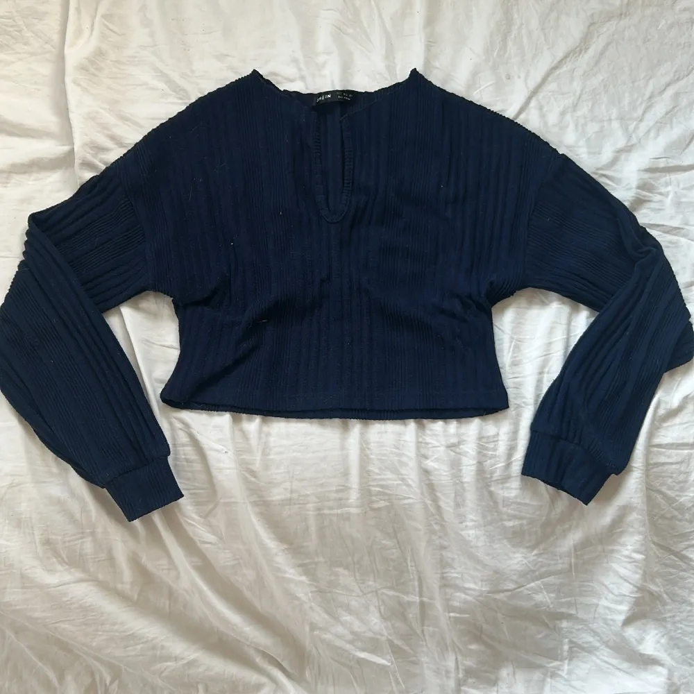 Säljer en mörkblå croppad tröja från NA-KD med ribbad struktur. Tröjan har långa ärmar och en liten v-ringning vid halsen. Perfekt till jeans eller kjol för en avslappnad look.. Neuletakit & Villapaidat.