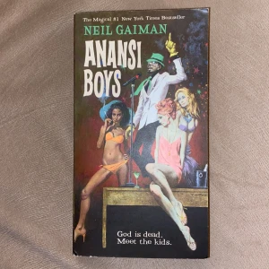 Anansi Boys - Säljer boken 'Anansi Boys' av Neil Gaiman. Omslaget har en färgstark illustration med en man i hatt och kostym samt två kvinnor. Boken är på engelska och utgiven av Morrow Fiction. Perfekt för dig som gillar fantasy och magisk realism.