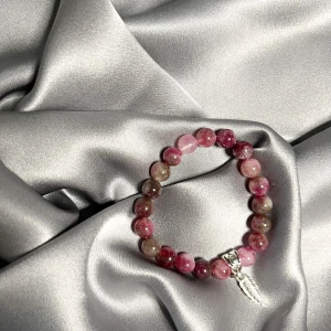 Rosa och lila armband med pärlor och berlock - Säljer ett armband med runda pärlor i olika nyanser av rosa, lila och vitt. Armbandet har en silverfärgad berlock i form av ett löv. Perfekt accessoar för att ge din outfit en färgklick.