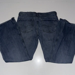 Blå jeansbyxor från Bershka - Säljer ett par klassiska blå jeans från Bershka med bootcut ben. Jeansen har normal passform, dragkedja och knapp framtill samt snygga sömdetaljer på bakfickorna. Perfekta till vardags och enkla att matcha.