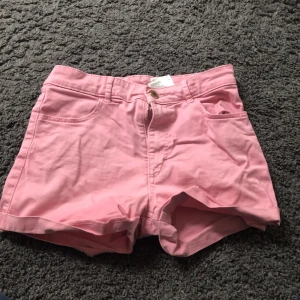 Rosa shorts från H&M - Säljer ett par ljusrosa shorts från H&M med klassisk femficksdesign och knappgylf. Shortsen har bälteshällor och är tillverkade i ett mjukt bomullsmaterial. Perfekta för varma dagar!