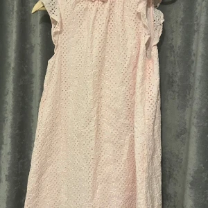 Ljusrosa spetsklänning från & Other Stories - Supersöt ljusrosa klänning från & Other Stories med broderad spets och volang vid halsringningen. Ärmlös modell med romantisk känsla, perfekt för sommarens alla tillfällen. Luftig och bekväm passform.