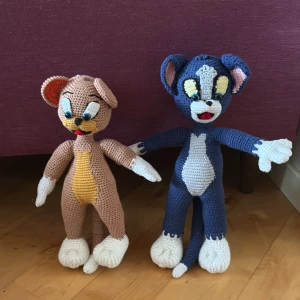 Virkade Tom och Jerry gosedjur - Handgjorda virkade gosedjur föreställande Tom och Jerry. Tom är blå och vit med gula detaljer, och Jerry är brun med beige mage och vita tassar. Båda har stora öron och broderade ansikten. Perfekta som unika accessoarer eller dekoration.