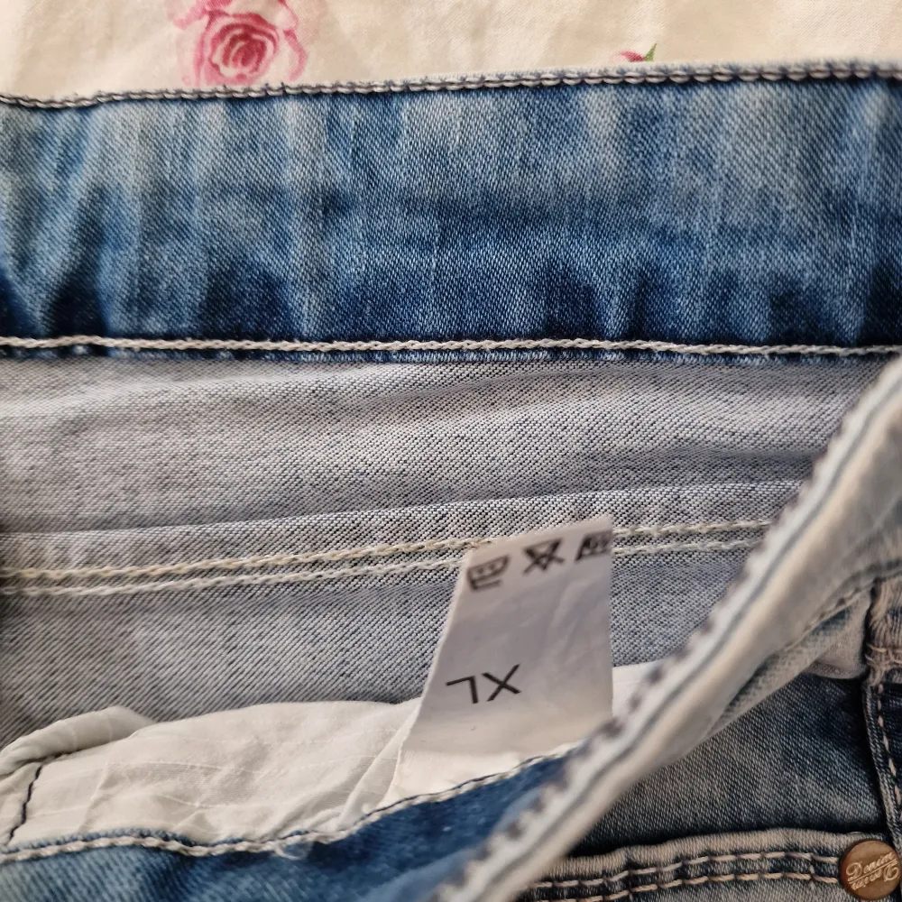 Snygg asymmetrisk jeanskjol i ljusblå denim med råa kanter och slitna detaljer. Kjolen har en unik design med snedskuren nederkant och klassiska femficksdetaljer. Perfekt för en trendig look! Ganska elastisk i storlek XL. Hameet.