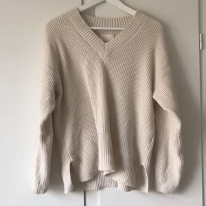 Beige stickad tröja med v-ringning - Säljer en mysig beige stickad tröja med v-ringning. Tröjan har långa ärmar och en avslappnad passform, perfekt för kyligare dagar. Den ribbade strukturen ger en stilren look. Strl s 36