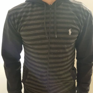Polo Ralph Lauren hoodie  - Svart och grå randig hoodie från Polo Ralph Lauren. Den har dragkedja framtill och en klassisk logga på bröstet. Storlek XL, passar mer som L..