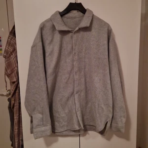 Grå Overshirt - Säljer en stilren grå overshirt med knappar framtill. Den har en klassisk krage och är tillverkad i ett mjukt material som ger en bekväm känsla. Perfekt för en fet grisch stil💯