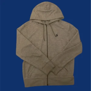 Grå hoodie från Polo Ralph Lauren - Säljer en stilren grå hoodie från Polo Ralph Lauren med dragkedja och justerbar huva. Tröjan har långa ärmar och en liten broderad logotyp på bröstet. Perfekt för en avslappnad look. Storlek M priset är inte hugget i sten vid snabb affär