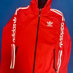 Röd träningsjacka från Adidas - Snygg röd träningsjacka från Adidas med dragkedja och huva. Jackan har vita detaljer och Adidas-logga på bröstet. Perfekt för sportiga aktiviteter eller en casual look. Priset går att diskutera 