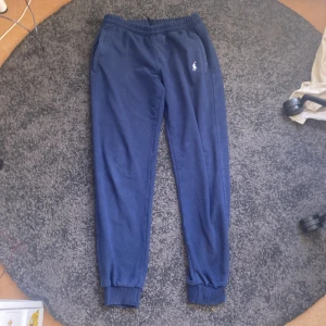 Ralph lauren byxor  - Säljer ett par bekväma blå mjukisbyxor från Polo Sport Ralph Lauren. Byxorna har en elastisk midja och muddar vid bensluten. Perfekta för en avslappnad stil.