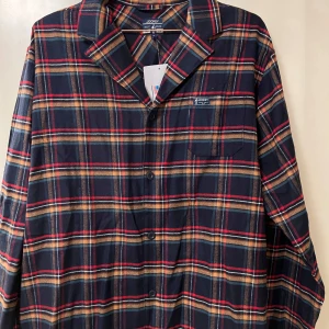 Rutig skjorta från Jockey  - Säljer en klassisk rutig skjorta i mörkblått, rött och beige från Jockey . Skjortan har lång ärm, knappar framtill och en bröstficka. Perfekt för dig som gillar en avslappnad men stilren look.