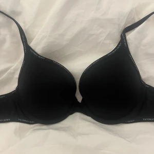 Svart push-up bh från Victoria's Secret - Säljer en svart push-up bh från Victoria's Secret. Den har en stilren design med märkets logga längs kanterna. Perfekt för att ge extra stöd och form under dina kläder. Den är använd men i mycket bra skick!