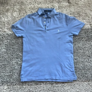 Blå pikétröja från Ralph Lauren - Hej! Säljer en stilren blå pikétröja från Ralph Lauren. Tröjan är i slim fit och har en klassisk krage med knappar. Perfekt för en avslappnad men ändå elegant look, särskilt för sommaren. Skriv gärna för fler frågor!