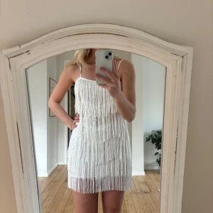 Vit klänning - Säljer en snygg vit klänning med fransar som ger en härlig rörelse. Klänningen är ärmlös med smala axelband och har en kort längd som passar perfekt för sommarens fester. Perfekt för dig som vill sticka ut!