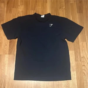 Svart t-shirt från Gymshark - Säljer en svart t-shirt från Gymshark med deras logga tryckt på bröstet. T-shirten har en klassisk passform och är perfekt för träning eller chill. Enkel och stilren design som funkar till det mesta.