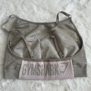 Grå sport-bh från Gymshark - Säljer en grå sport-bh från Gymshark med justerbara axelband och logga framtill. Mjuk och stretchig modell som passar perfekt till träning.