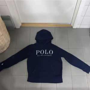 Mörkblå hoodie från Ralph Lauren - Säljer en snygg mörkblå hoodie från Ralph Lauren med stor POLO-logga på bröstet. Tröjan har långa ärmar och en klassisk huva. Perfekt för en avslappnad stil. Köpt i usa