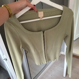 Khaki ribbad kofta - Säljer en ribbad kofta i khaki från H&M. Den är croppad med ”hakar” framtill och har långa ärmar. En korsettliknande topp som sitter tajt runt kroppen. Superfin men kommer tyvärr inte till användning. Använd en gång.