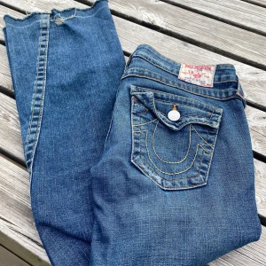 Blå jeans från True Religion - Säljer ett par klassiska blå jeans från True Religion med ikonisk bakficka. Jeansen har normal passform och bootcut. Tillverkade i USA och har snygga detaljer som logoknapp och tydliga sömmar.