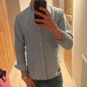 Ljusblå skjorta från Ralph Lauren - Säljer en stilren ljusblå skjorta från Ralph Lauren. Skjortan har långa ärmar och knappar framtill. Perfekt för en klassisk och elegant look. Säljer då den är alldeles för liten på mig.