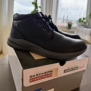 Skor Herr Skechers - Säljer ett par bekväma och vattentäta skor – Skechers Delson 3.0 Brandis. Perfekta för promenader i alla väder. Skorna har stötdämpande mellansula och en mjuk Memory Foam-innersula som formar sig efter foten för maximal komfort. Sköna att ha på hela dagen – både praktiska och snygga. Storlek 42. De är helt oanvända & kartong finns med 💙