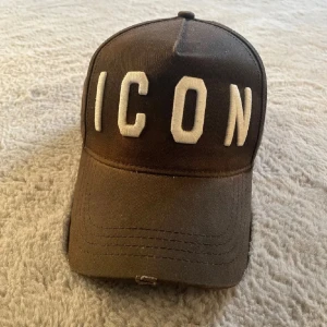 Svart keps från Dsquared2 med broderad text - Säljer en svart keps från Dsquared2 med stor vit broderad text 'ICON' framtill och 'DSQUARED2' baktill. Justerbar passform och klassisk böjd skärm. Perfekt accessoar för en trendig streetwear-look. Köpte på NK i Stockholm för 1400kr. Kepsen ha blivit lite solblekt, därav priset!! Skriv vid minsta fundering. Priset kan diskuteras vid snabbaffär!! KVITTO FINNS